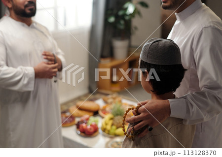 Selective focus shot of proud Muslim father and his son talking to male relative at family gathering on Eid Al-Fitr, copy space 113128370