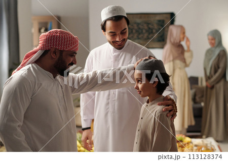 Cheerful bearded Middle Eastern man patting his nephew on head at family gathering on Uraza Bayram day 113128374