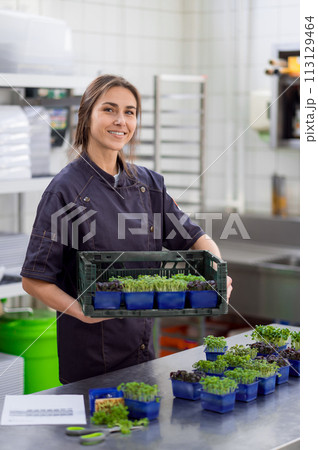 Woman in uniform holding microgreens in restaurant kitchen 113129464