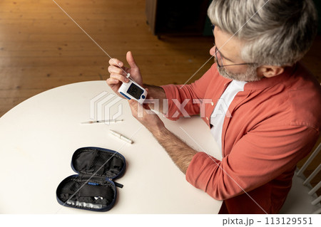 Middle aged man with glucometer checking blood sugar level at home 113129551