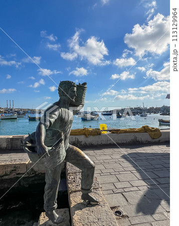 A wonderful monument on the shore of Marsaxlokk, Malta: a young son and daughter meet a father who is carrying two wicker baskets full of caught fish. 113129964