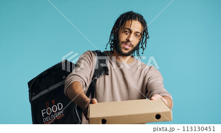 Portrait of BIPOC courier delivering pizza order to client. Delivery part time worker using thermal backpack to store food and bring it to customer, isolated over studio background, camera A Portrait of BIPOC courier delivering pizza order to client. Delivery part time worker using thermal backpack to store food and bring it to customer, isolated over studio background, camera A 113130451