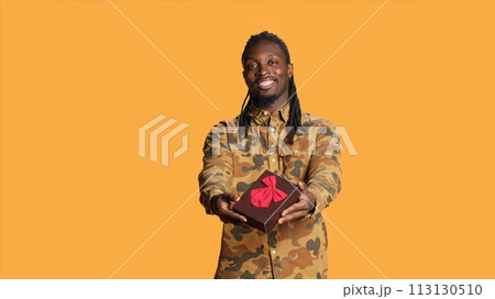 African american person offering giftbox to his girlfriend, giving present packed with ribbon and bow on camera. Young adult doing cute romantic gesture on their anniversary or valentines day. African american person offering giftbox to his girlfriend, giving present packed with ribbon and bow on camera. Young adult doing cute romantic gesture on their anniversary or valentines day. 113130510