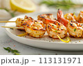Grilled shrimp with lemon and fresh herbs on white plate, with a sprinkle of spices creating an elegant presentation 113131971