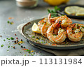 Char-grilled shrimps seasoned with herbs on a rustic ceramic plate, adorned with a wedge of lemon, on a gray 113131984