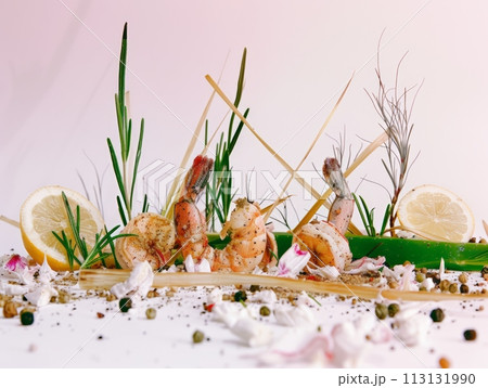 grilled shrimp on skewers with lemon slices, garnished with fresh herbs and spices on a light background. 113131990