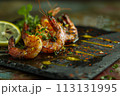 Close-up of charred shrimps with vibrant spices on a black slate, garnished with fresh herbs and lemon. 113131995