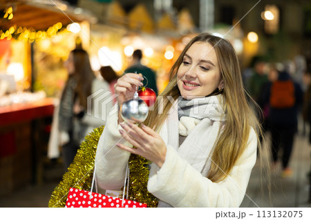 Smiling woman is buying Christmas balls for X-mas tree in market outdoor Smiling woman is buying Christmas balls for X-mas tree in market outdoor 113132075