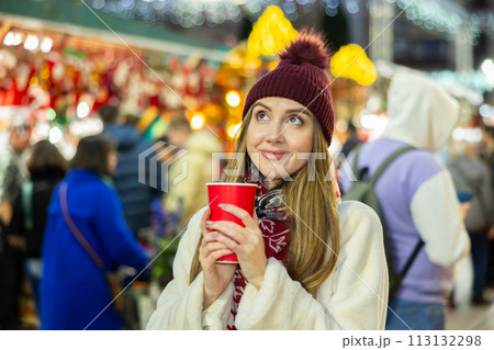 Young woman stands with glass of hot coffee in her hands and enjoys festive New Year atmosphere Young woman stands with glass of hot coffee in her hands and enjoys festive New Year atmosphere 113132298