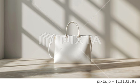 A white purse with a gold strap sits on a table in front of a plant 113132598