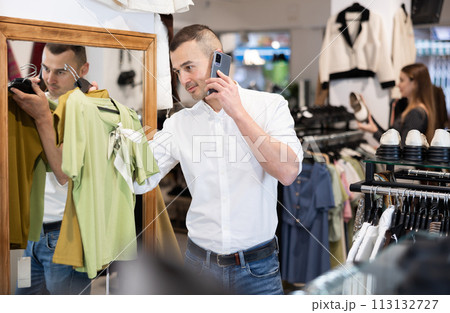 While shopping, man chooses gift, examines womans blouse and talks on phone While shopping, man chooses gift, examines womans blouse and talks on phone 113132727