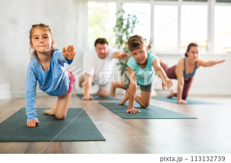 Pleasant little girl practicing table pose of yoga with her family Pleasant little girl practicing table pose of yoga with her family 113132739