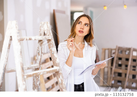 Brown-haired young woman with papers planning upcoming home overhaul Brown-haired young woman with papers planning upcoming home overhaul 113132758