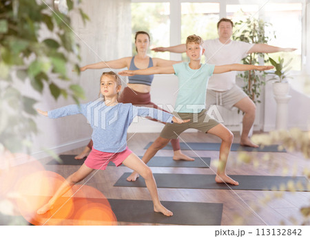 Pleasant little girl practicing warrior pose of yoga with her family Pleasant little girl practicing warrior pose of yoga with her family 113132842
