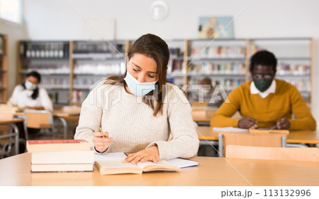 Woman wearing mask studying in public library Woman wearing mask studying in public library 113132996