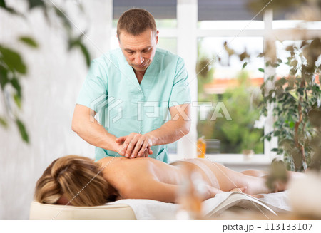 Woman enjoys back massage during spa treatments at cosmetology center Woman enjoys back massage during spa treatments at cosmetology center 113133107