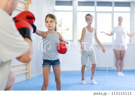 Girl and dad are boxing in gym, father helps child to work out force of blow. 113133113