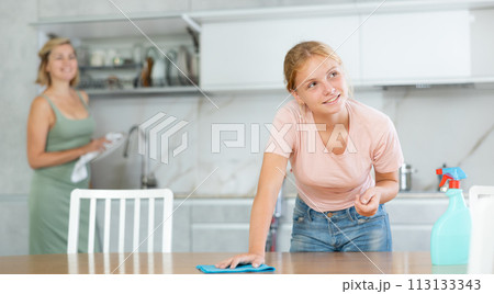 Teen girl help mother and wash dining table in kitchen, blurry mom cleaning using vacuum cleaner Teen girl help mother and wash dining table in kitchen, blurry mom cleaning using vacuum cleaner 113133343