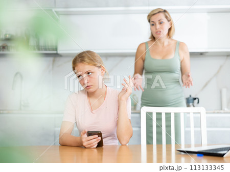 Teenage girl with smartphone making dismissive gesture to mother Teenage girl with smartphone making dismissive gesture to mother 113133345