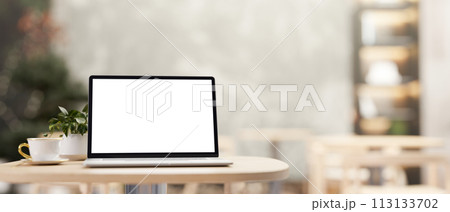 A white-screen laptop computer mockup on a wooden table in a cozy contemporary coffee shop cafe. A white-screen laptop computer mockup on a wooden table in a cozy contemporary coffee shop cafe. 113133702