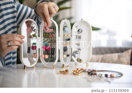 A young woman chooses earrings for herself. Storage of jewelry and costume jewelry. 113139369