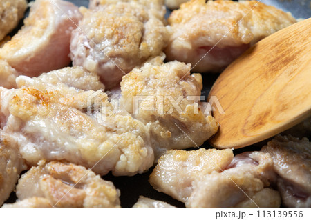 鶏肉(片栗粉をまぶした鶏モモ肉)をフライパンで炒める調理シーン。 113139556