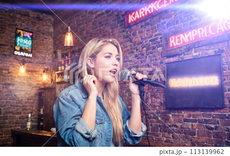 Woman singing karaoke in microphone. happy young women singing karaoke in bar. woman singing in night bar on weekend. concept with young woman in bar 113139962