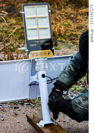 Assembly of fully autonomous, standalone LED street lighting, construction worker install support bracket to wooden pilon. Assembly of fully autonomous, standalone LED street lighting, construction worker install support bracket to wooden pilon. 113142173