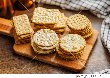 A stack of crackers neatly arranged on cutting board on wooden tabletop. A stack of crackers neatly arranged on cutting board on wooden tabletop. 113144582