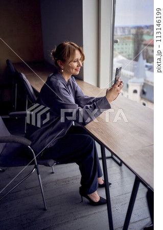 beautiful middle age business woman wearing gray shirt, wide leg pants abd black stilettos make video for a stories in moders workspase in tall building beautiful middle age business woman wearing gray shirt, wide leg pants abd black stilettos make video for a stories in moders workspase in tall building 113146199