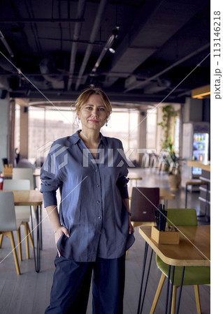 an           attractive middle age woman with crossed arms in a modern coworking neutral design, wearing wide leg pants and a silk blouse 113146218