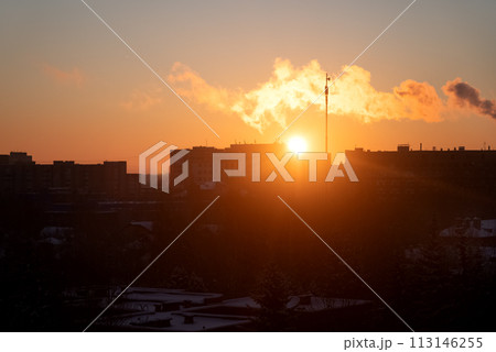 Smoke from the plant pipes or chimney stretches over the roofs of houses in residential area against sunset sky 113146255