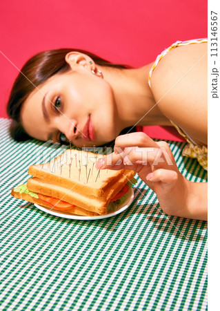 Young woman lying next to sandwich with pins resembling acupuncture against pink background. Meditation Young woman lying next to sandwich with pins resembling acupuncture against pink background. Meditation 113146567
