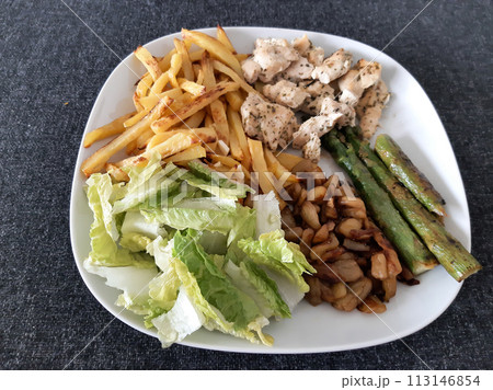 Homemade grilled chicken with french fries, asparagus, grilled chopped eggplant and green salad, served on a white plate 113146854