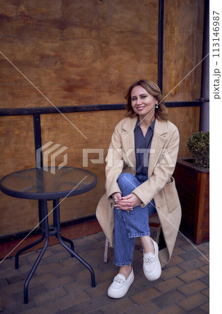 young adult woman in jeans and sand coat with grunge background, rusty wall with coffee lettering young adult woman in jeans and sand coat with grunge background, rusty wall with coffee lettering 113146987