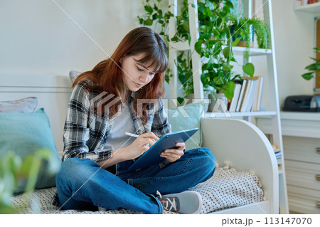 Young female teenager with digital tablet, stylus drawing illustrating sitting on couch at home Young female teenager with digital tablet, stylus drawing illustrating sitting on couch at home 113147070