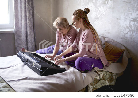 A 60-year-old mother and a 40-year-old daughter play the keyboard together on the bed at home A 60-year-old mother and a 40-year-old daughter play the keyboard together on the bed at home 113147680