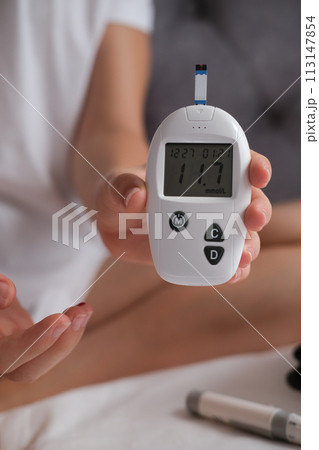 Teenage girl measures blood glucose level on bed at home. Teenage girl measures blood glucose level on bed at home. 113147854