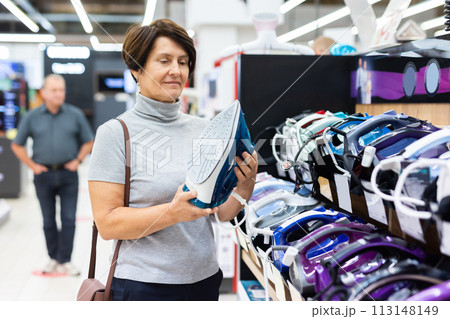 Older woman picking out new clothes iron to buy in electronics department of supermarket Older woman picking out new clothes iron to buy in electronics department of supermarket 113148149