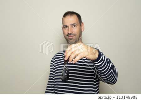 Bearded Hispanic man in his 40s wearing striped sweater, hold car key, keyless system, look at camera isolated on plain beige background studio portrait. People lifestyle concept. Selective focus. 113148988