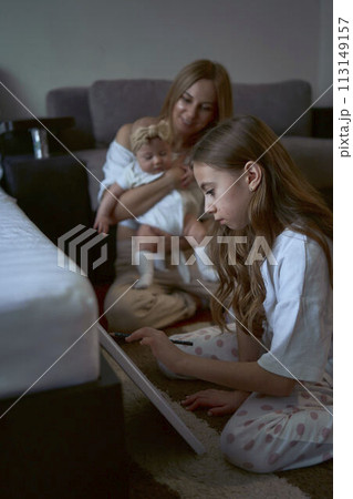 girl paint on the floor while her mother plays with baby sister 113149157