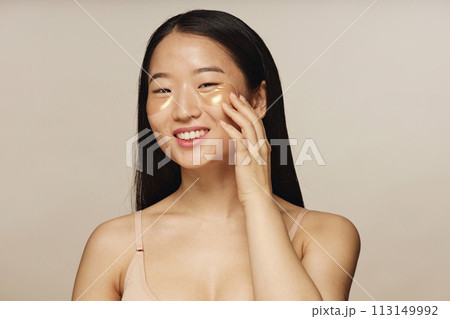 Medium closeup studio shot of young Asian woman posing for camera with collagen patches under eyes 113149992