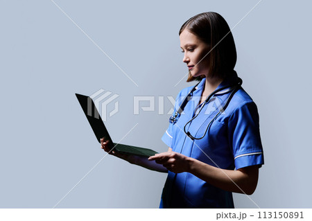 Female nurse using laptop, profile view on gray studio background 113150891