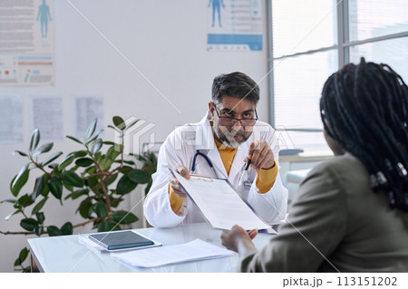 Portrait of senior Middle Eastern doctor handing documents to patient across table copy space Portrait of senior Middle Eastern doctor handing documents to patient across table copy space 113151202