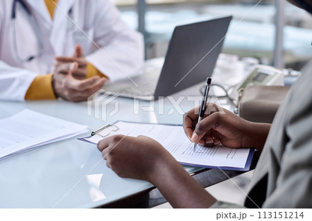 Close up of unrecognizable Black woman writing on clipboard in clinic filling in patients records copy space 113151214