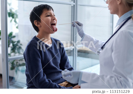 Side view closeup of female doctor doing throat swab of young boy sitting in exam room with open mouth copy space Side view closeup of female doctor doing throat swab of young boy sitting in exam room with open mouth copy space 113151229