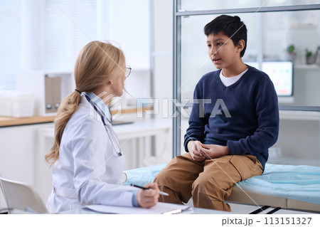 Portrait of young boy talking to doctor in clinic and explaining symptoms during check up examination 113151327