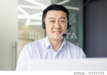 A professional Asian man is engaged in his work at a modern office, embodying dedication and focus. 113151726