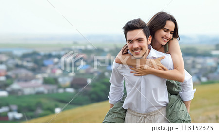 Man runs with girlfriend on back up hill overlooking village Man runs with girlfriend on back up hill overlooking village 113152325