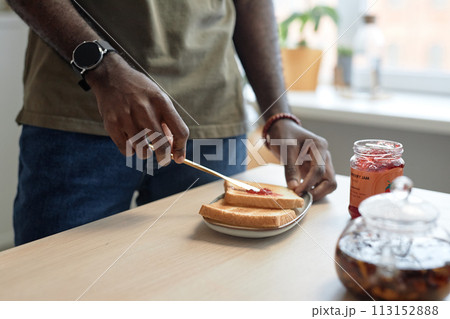 Close up of unrecognizable African American man making peanut butter and jelly sandwich at kitchen table for breakfast copy space 113152888